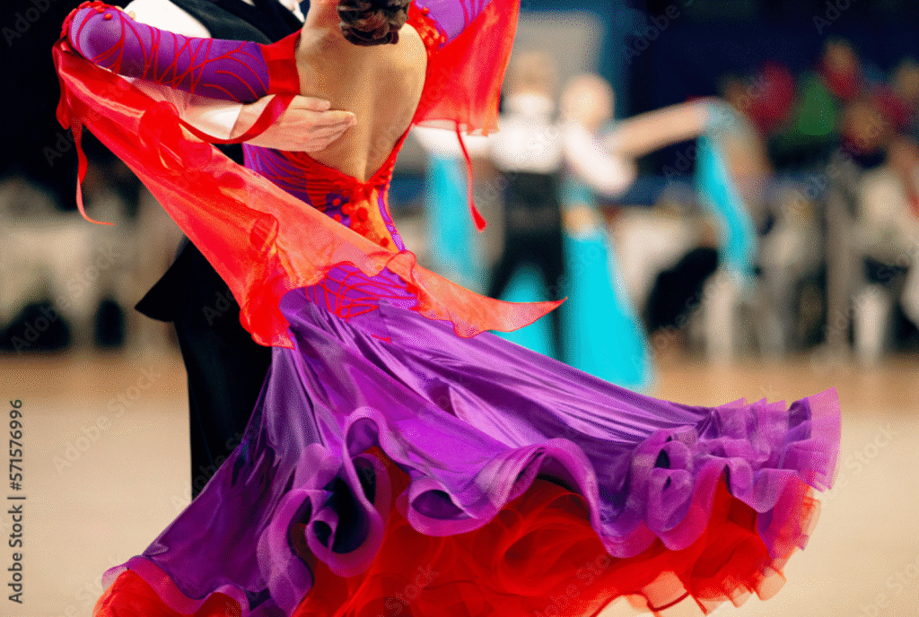 Ballroom dancers in close embrace; female dancer in purple and red dress with flared skirt, male dancer in black suit during a formal dance event
