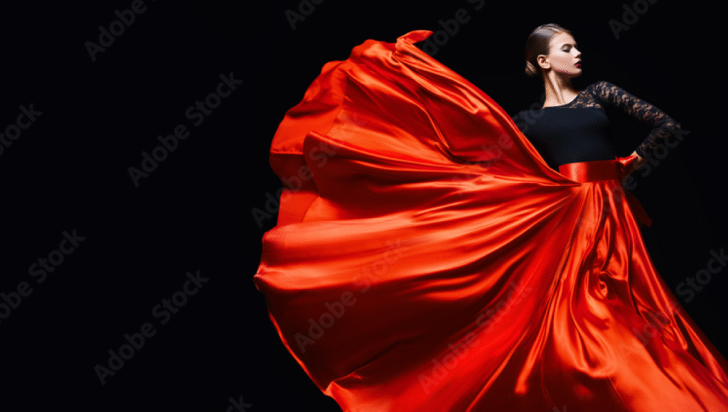 Person wearing a flowing red satin skirt and black lace-sleeved top, captured mid-motion against a black background.