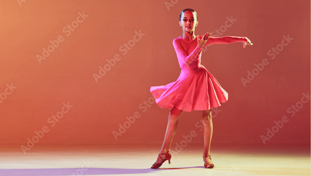 Young girl in a bright pink long-sleeved dance dress performing a spin, with the flared skirt captured mid-motion against a red-orange gradient background.