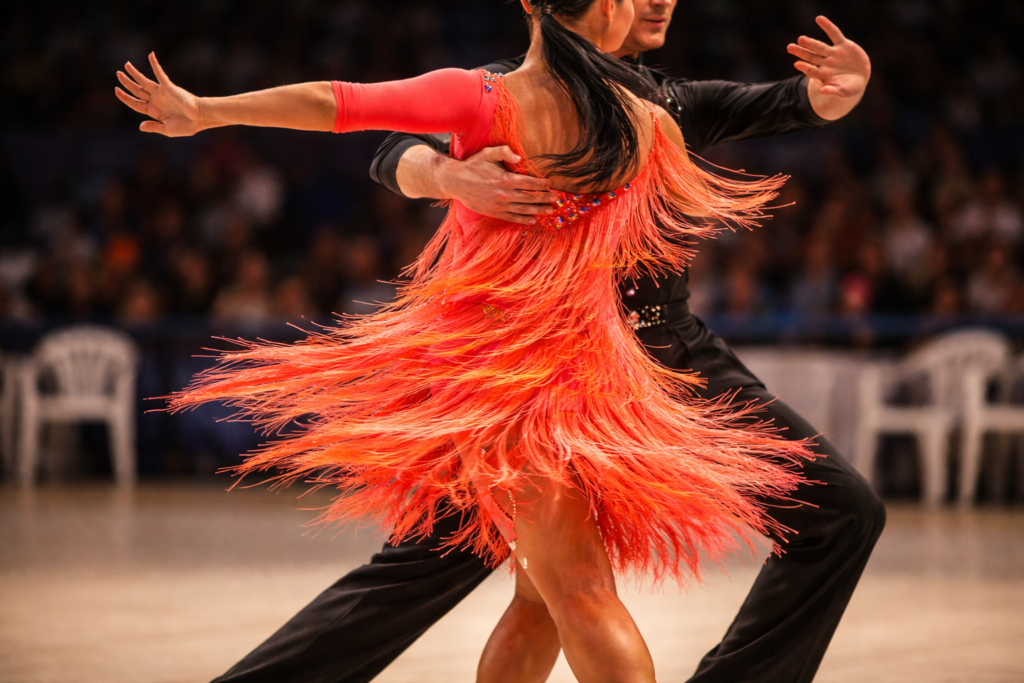 Female ballroom dancer wearing a vibrant orange Latin dress with fringe details during a performance