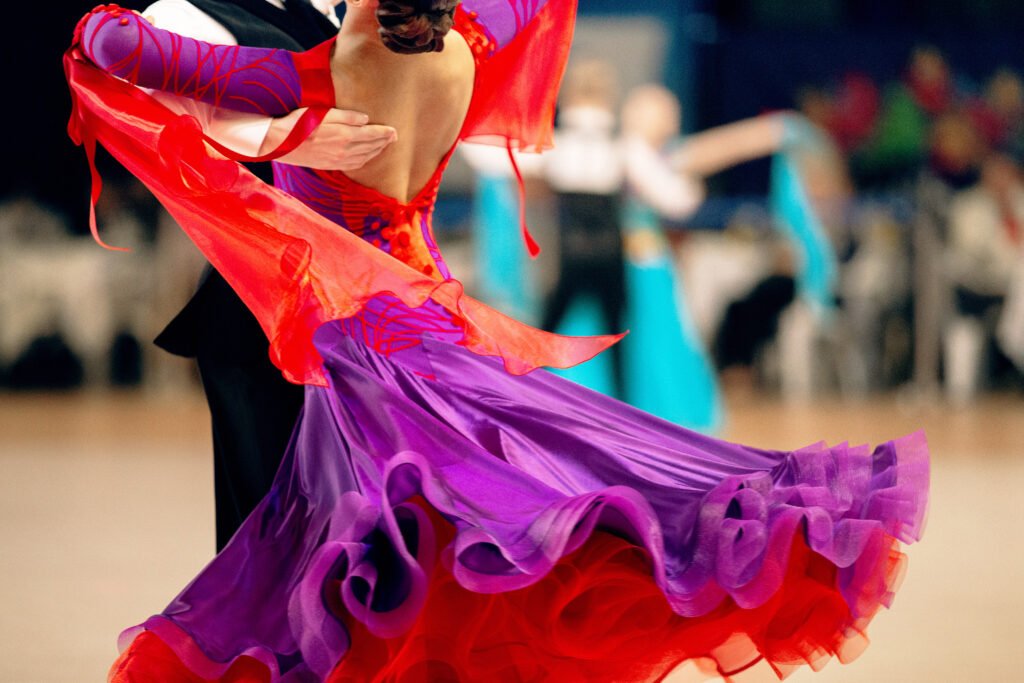 Ballroom dancers in close embrace; female dancer in purple and red dress with flared skirt, male dancer in black suit during a formal dance event